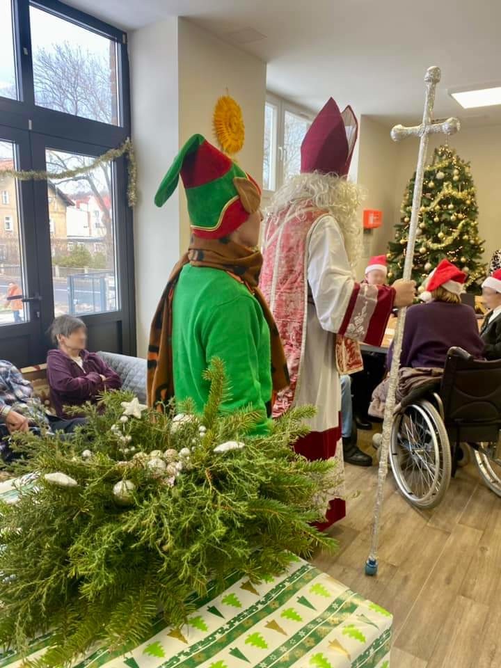 Przedstawia Mikołaja i elfa wraz z prezentem i stroikiem dla seniorów w domu pomocy społecznej